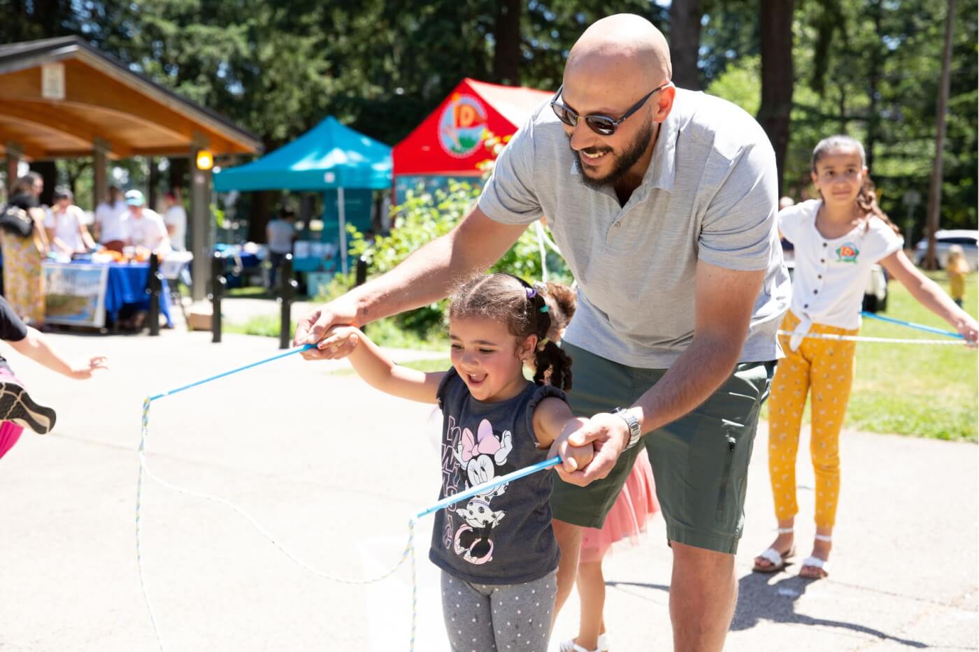 father helping little girl blow giant bubbles with a bubble wand comprised of string between two sticks