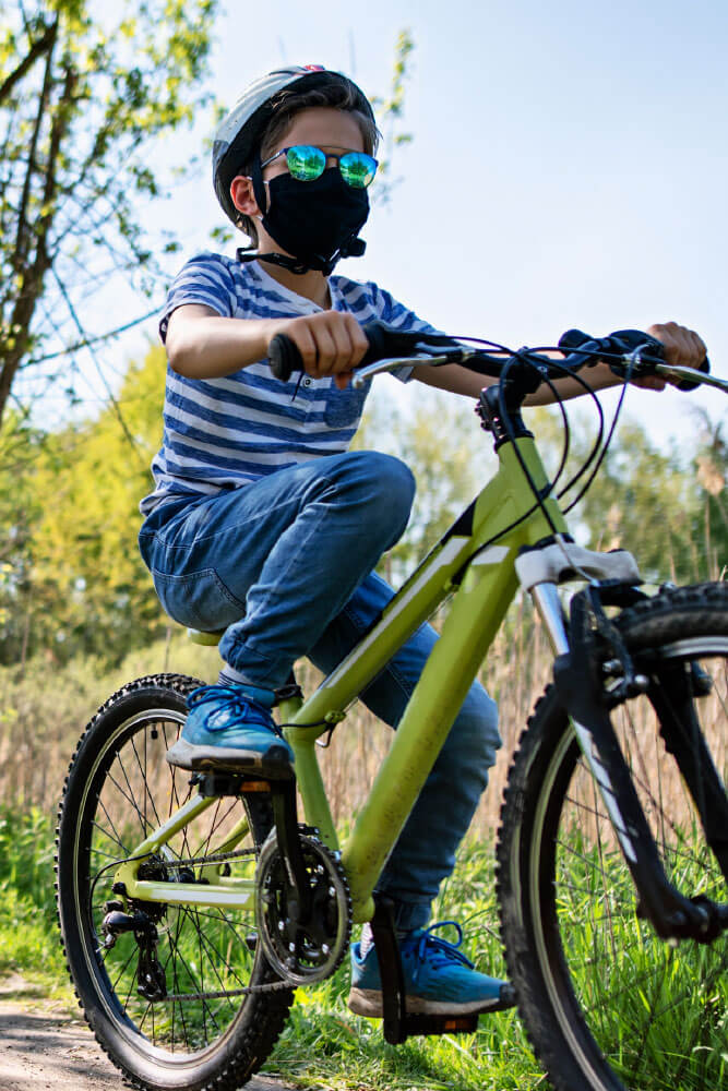 Boy riding bicycle while wearing a helmet and mask on a trail.