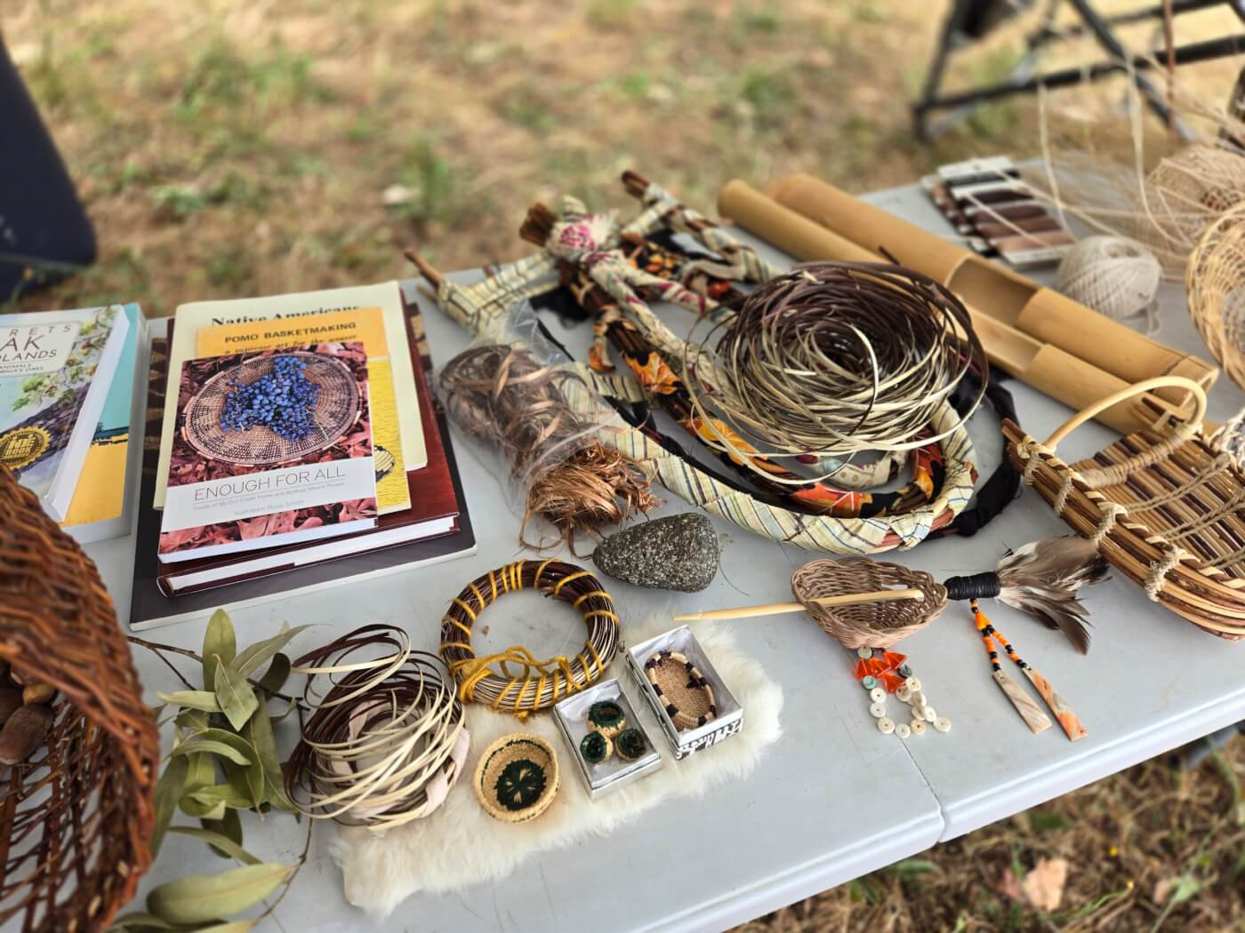 Cultural display table with miniature Pomo baskets, baby baskets, traditional medicines, clapper sticks and plant books.