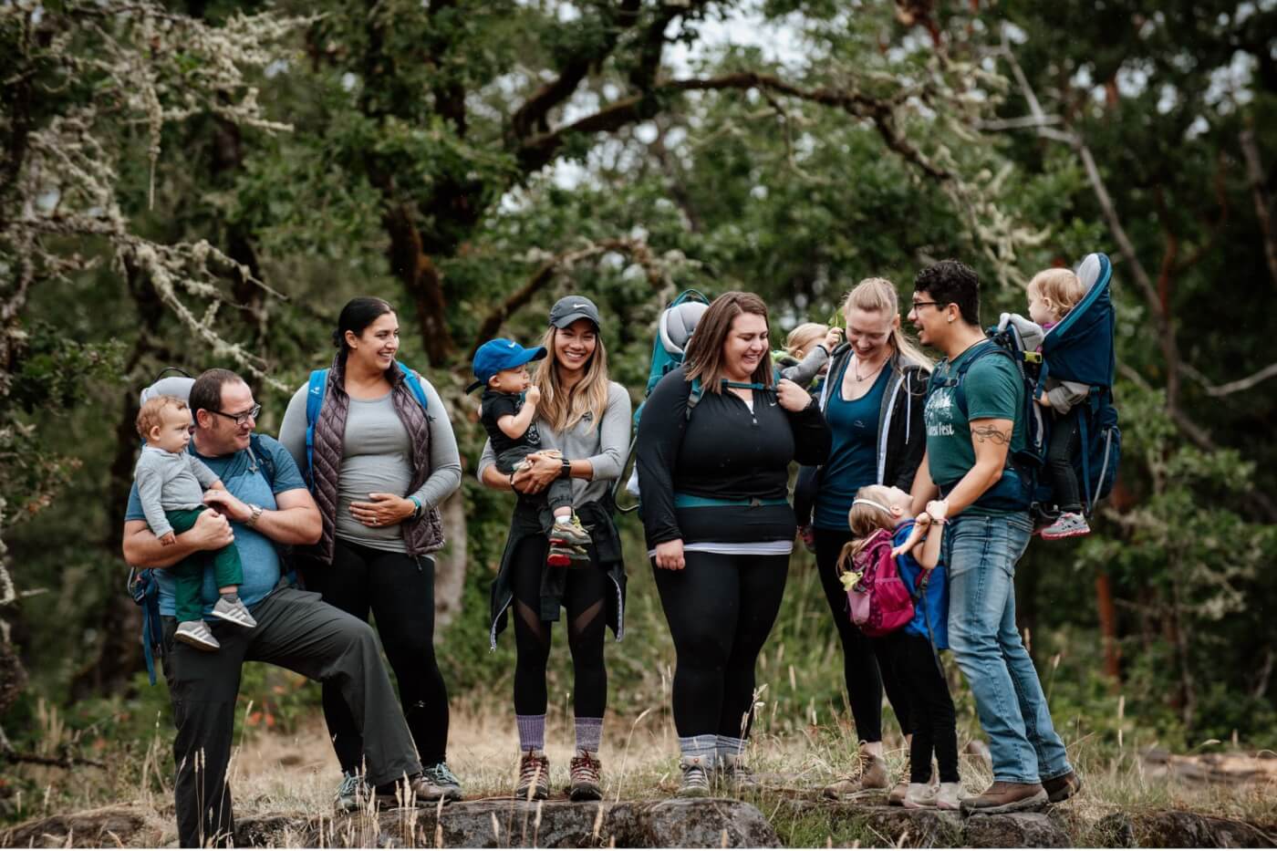 group of parents, mothers and fathers, hiking in the woods with their children with various carrying methods