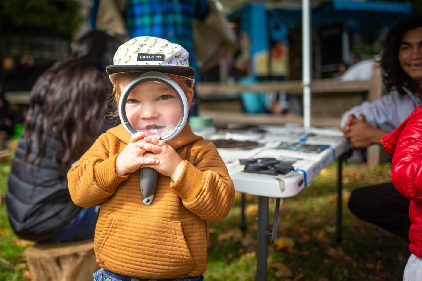 A young child peers through a magnifying glass at the camera, so their face is magnified.