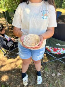 A Native youth standing outside, holding a small, hand-woven basket.