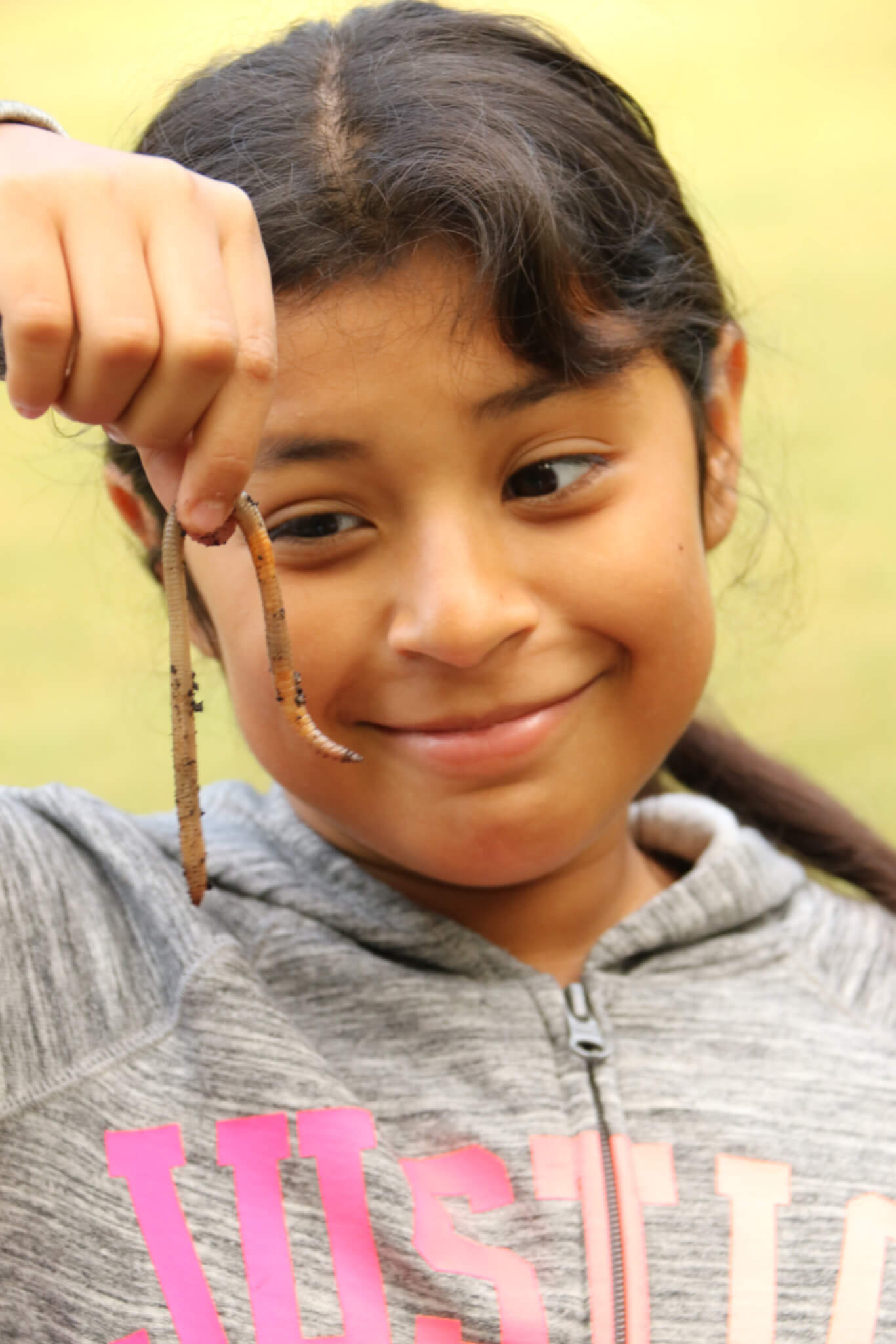 girl holding up a wiggly worm and smiling at the worm