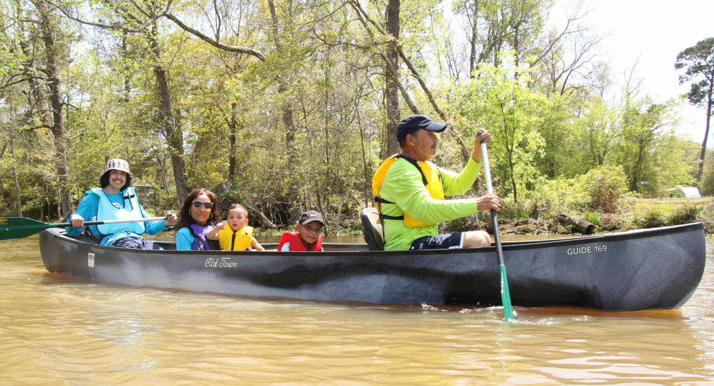 family in canoe paddling down river smiling at the camera