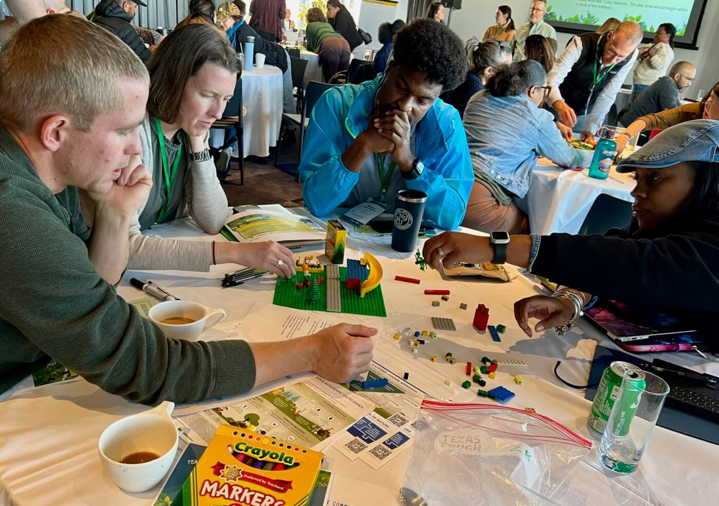 people sitting at a round table, stacking legos as part of the Nature everywhere vision lab