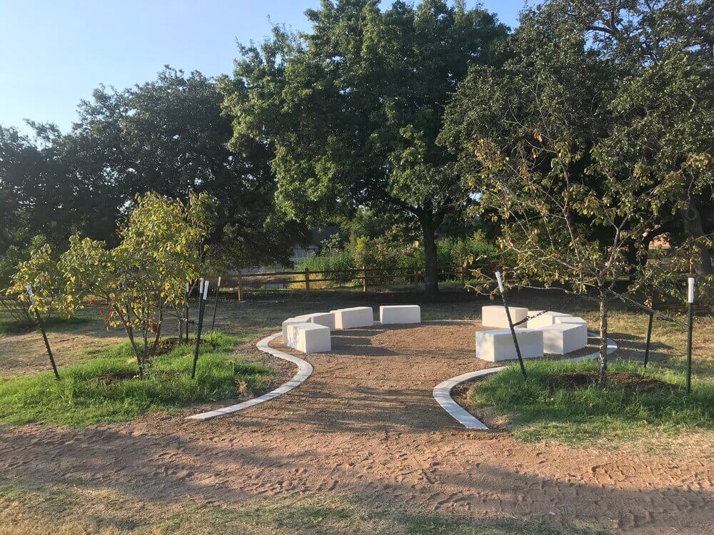 Ten stone slabs are situated in a circle, shaded by several mature and newly planted trees.