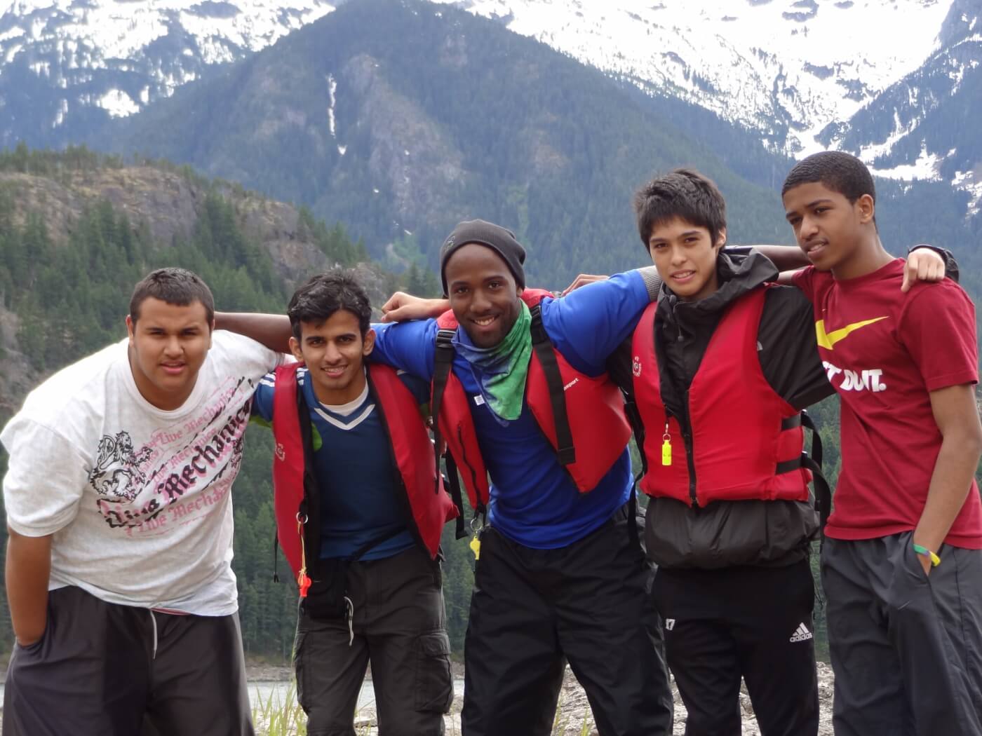 CJ Goulding poses with four students, some of whom wear life jackets, in front of a mountainous landscape.