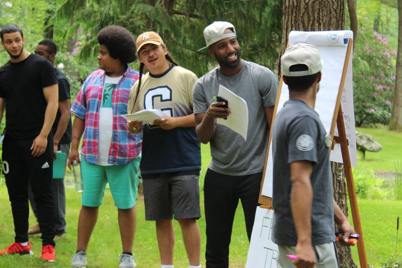 CJ Goulding stands outside with a group. He is leading an activity with an easel and notepad.