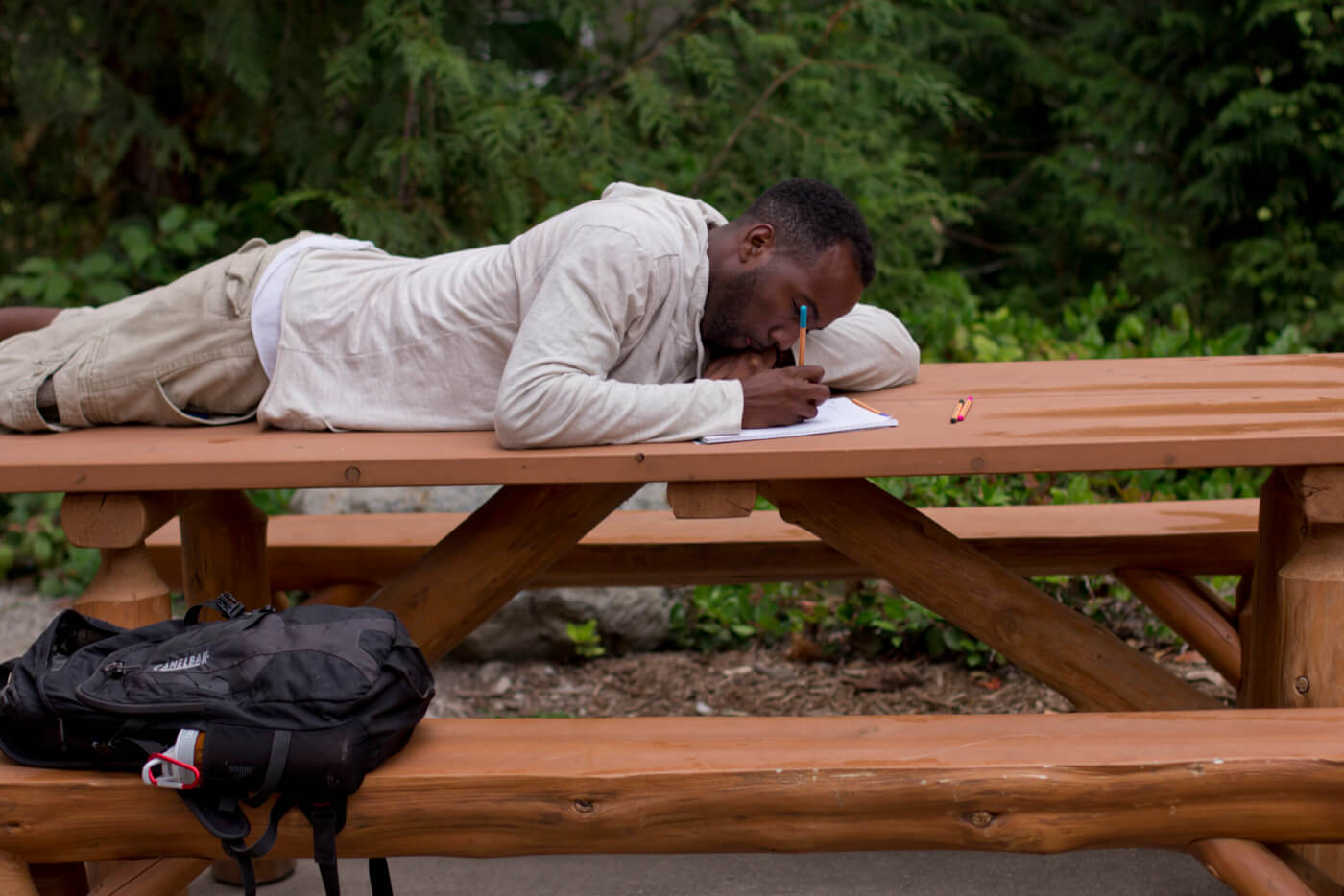 CJ Goulding writes in a notebook. He is lying on his stomach, on top of a picnic table.