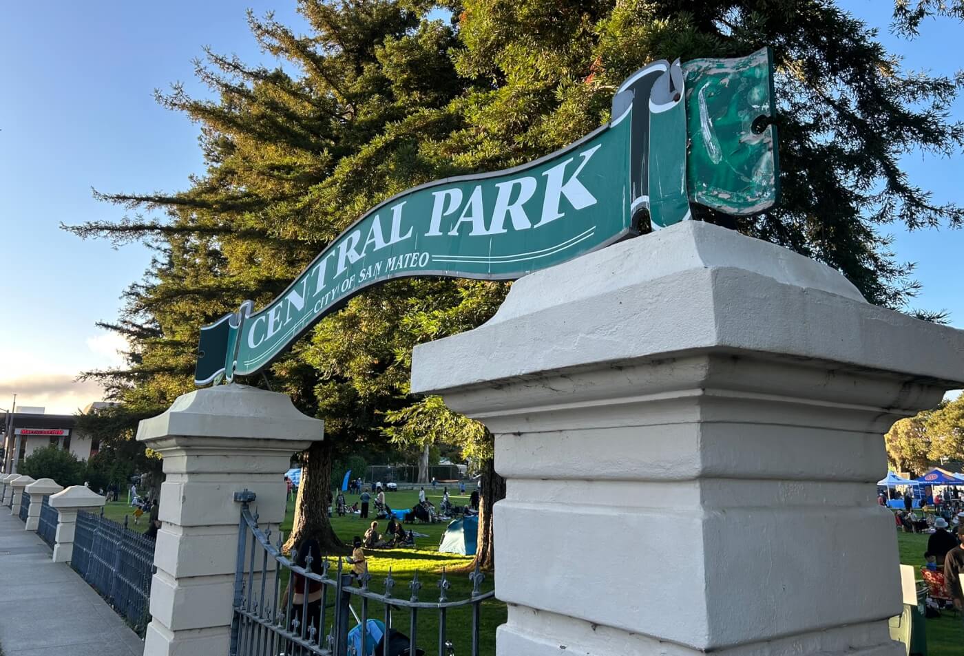 A green sign fashioned to look like a banner has the words “Central Park, City of San Mateo.” The sign is over large metal gates.