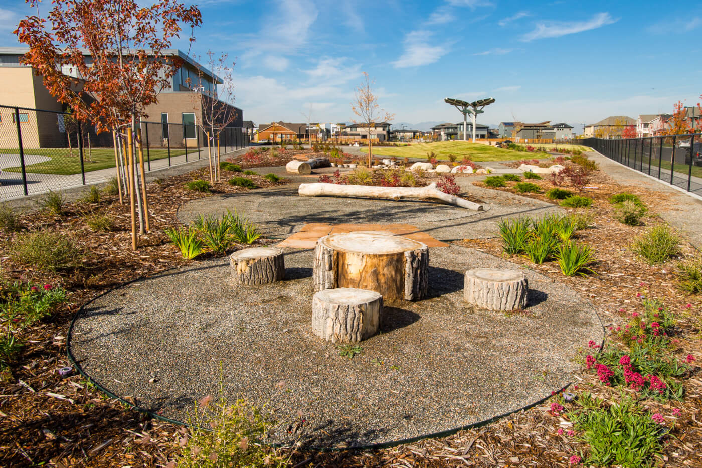 A Nature Exploration Area features a sitting area built from three tree stumps circling a larger tree stump. The area is ringed with a border of mulch and flowers.