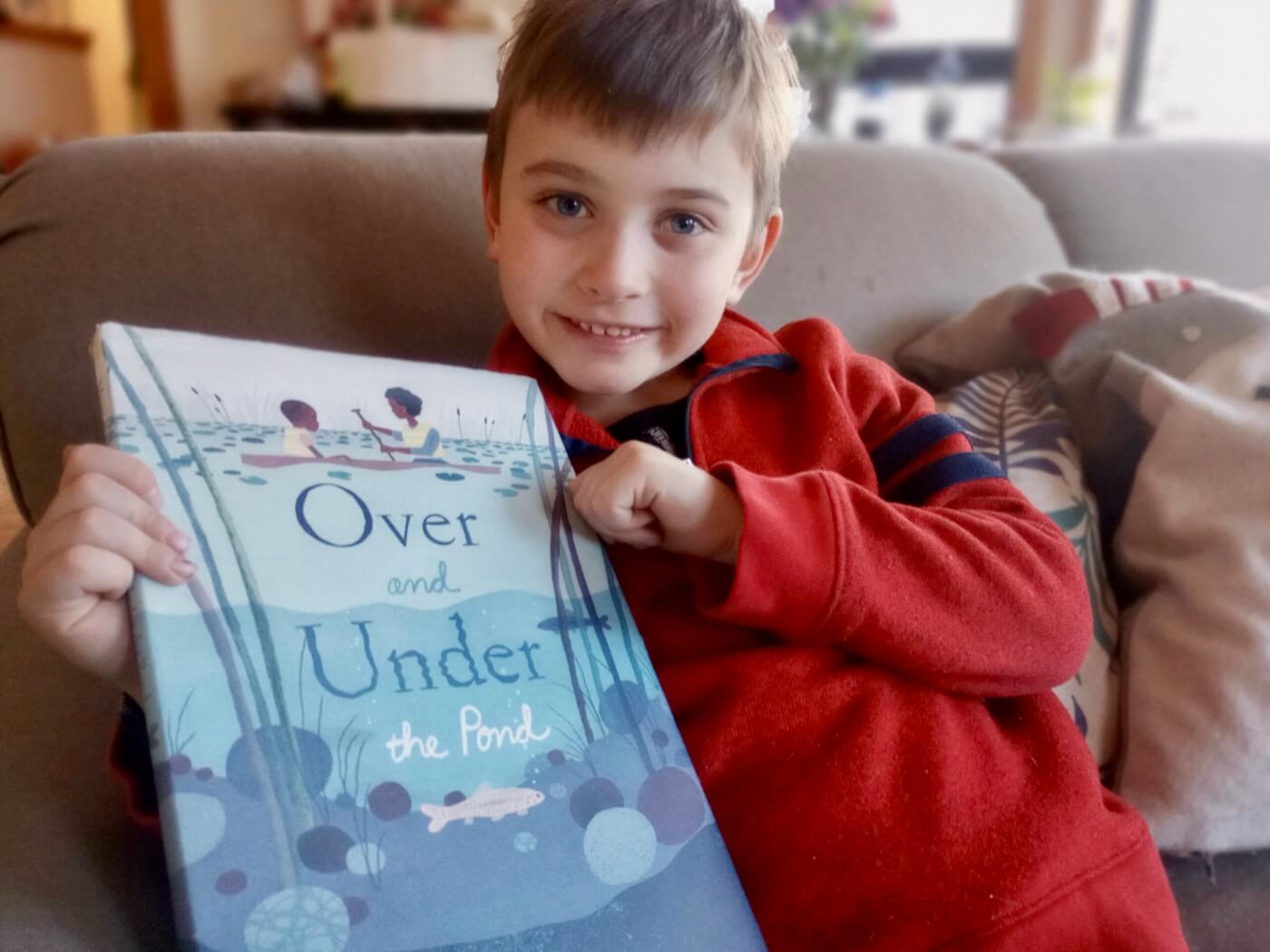photo of young boy sitting on the couch holding up a book that says, "Over and Under The Pond"