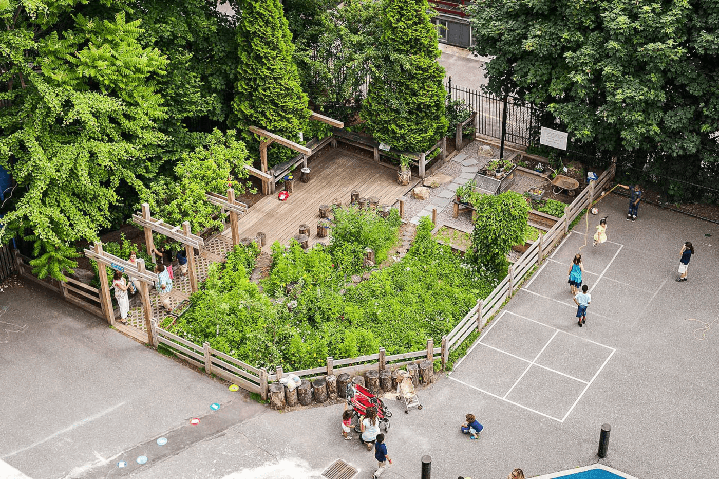 A bird’s-eye view of a green schoolyard featuring a trail winding through dense vegetation, raised garden beds and a seating area made of stumps. The area is bordered by a concrete play space.