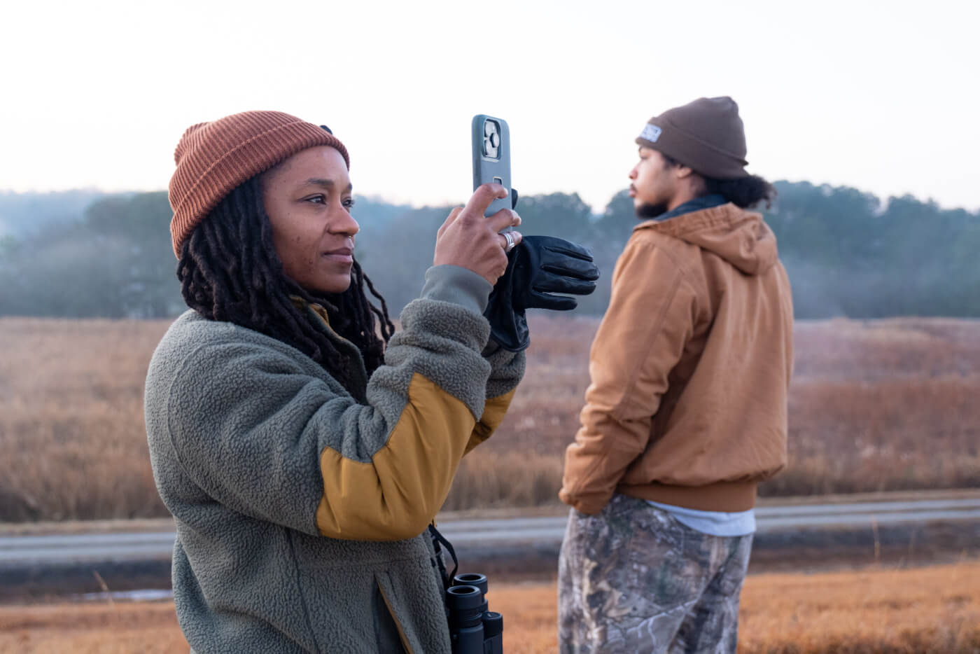 Devin Cowens, with her iPhone raised, taking pictures. A fellow birder is in the background.