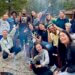 Group of young leaders surrounding a campfire smiling at camera.