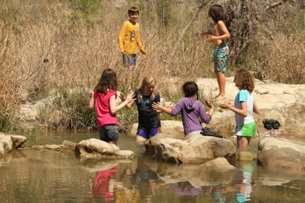 Kids playing in river by rocks.