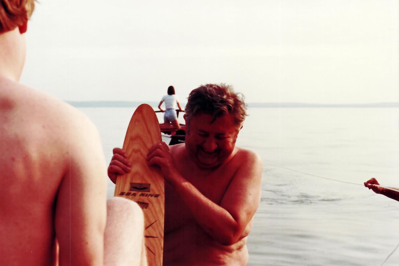An older, smiling man helps a young boy put water skis on his feet.