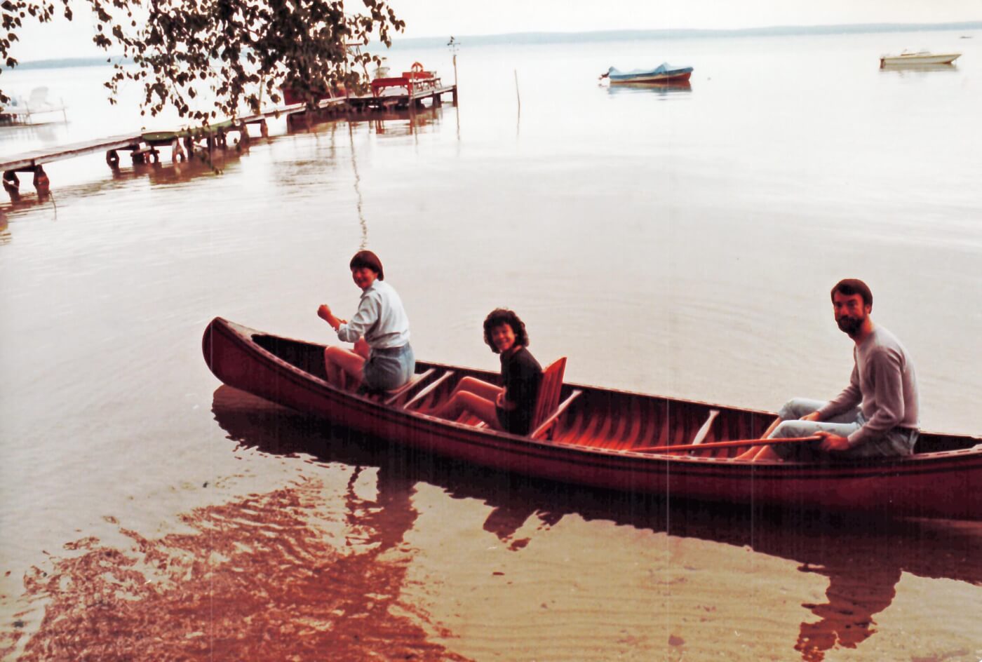 A man, a woman, and a young girl sitting in a red canoe on a lake.