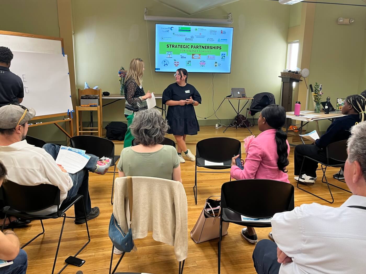 People attending a workshop presentation on “Strategic Partnerships for Greener Schools” in a meeting room.