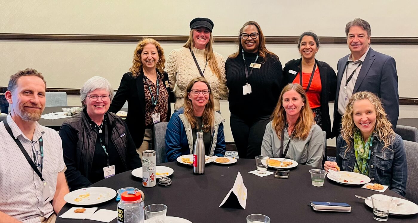 Group of conference attendees smiling around a table during a networking or meeting session.
