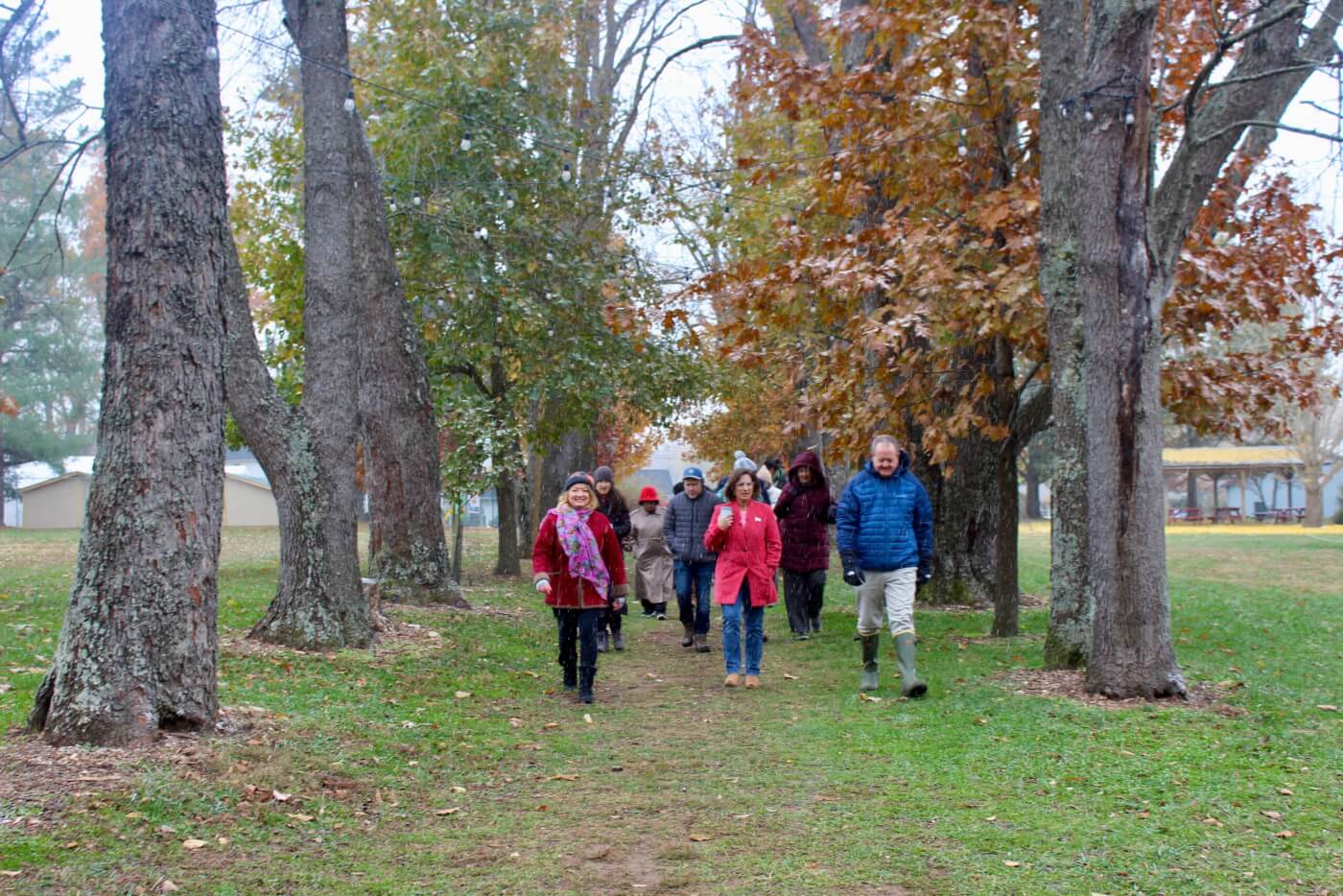 Group of adults walking together along a tree-lined path in a park during autumn.
