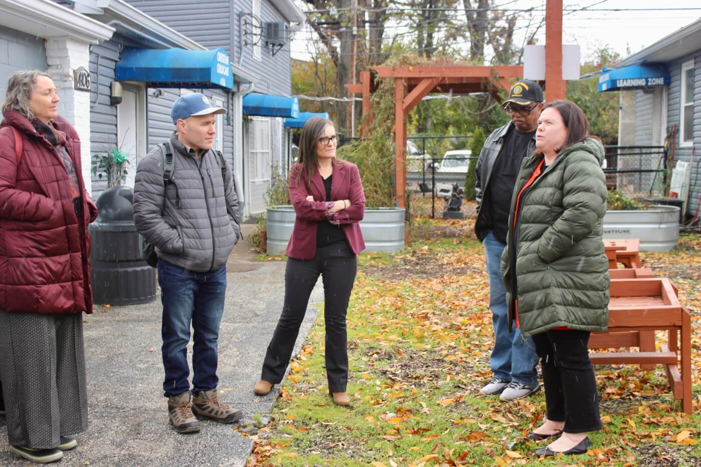 Group of adults standing outdoors and listening during a conversation outside a building.