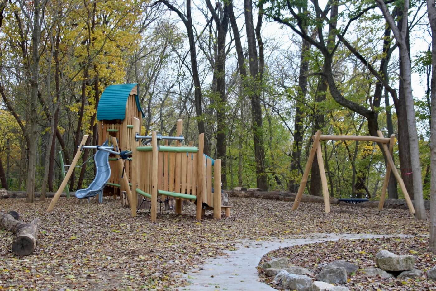 Wooden playground structure with a slide and swing set surrounded by trees in a natural outdoor setting.