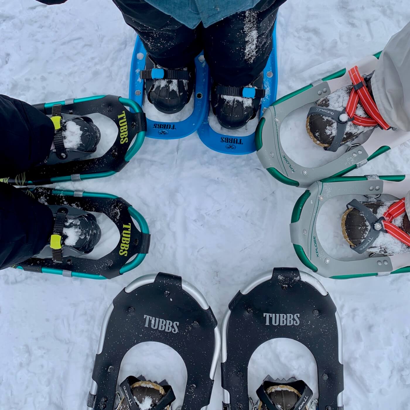 Photo of four people wearing snowshoes, feet only, facing one another in a circle