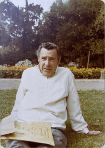 A vintage photograph of an older man in a white shirt, sitting on a lawn.