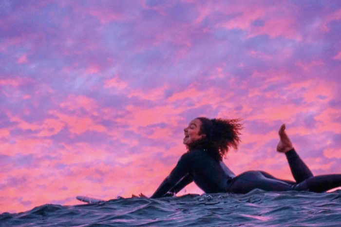 Inside-Out’s Youth Advisory Council member Kimiko Russell-Halterman smiles while surfing during sunset.