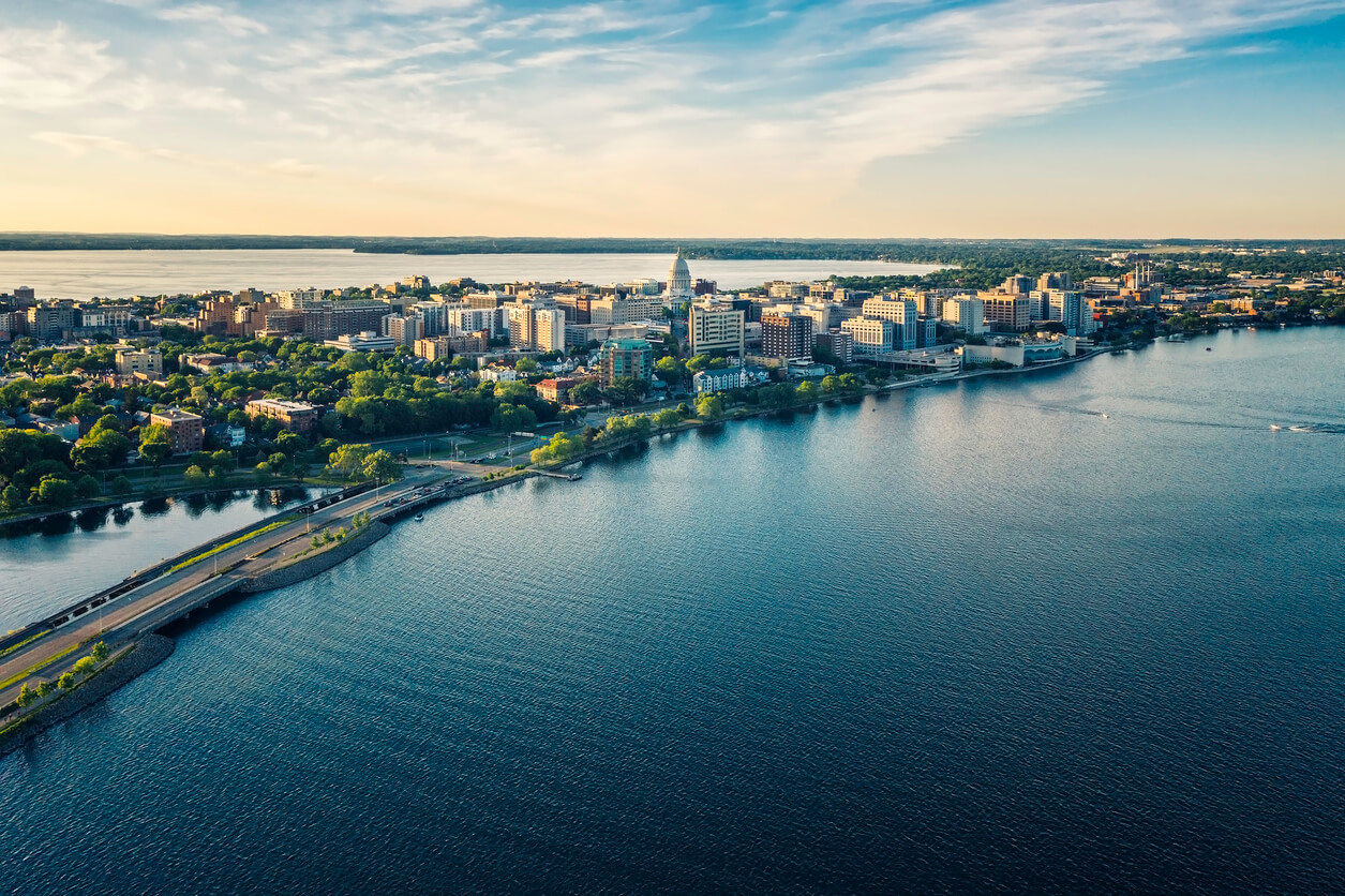 Aerial shot of a city during early sunset, situated between two lakes on an isthmus. The capitol building is notably centered in the skyline.