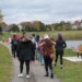 A group of adults and children walked down a paved trail next to a park bench and body of water in a park around Madison, Wisconsin