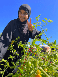 A participant holds up a peace sign in front of a tomato plant.