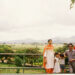 Family of five posing by a railing with a green landscape and mountains in the background.