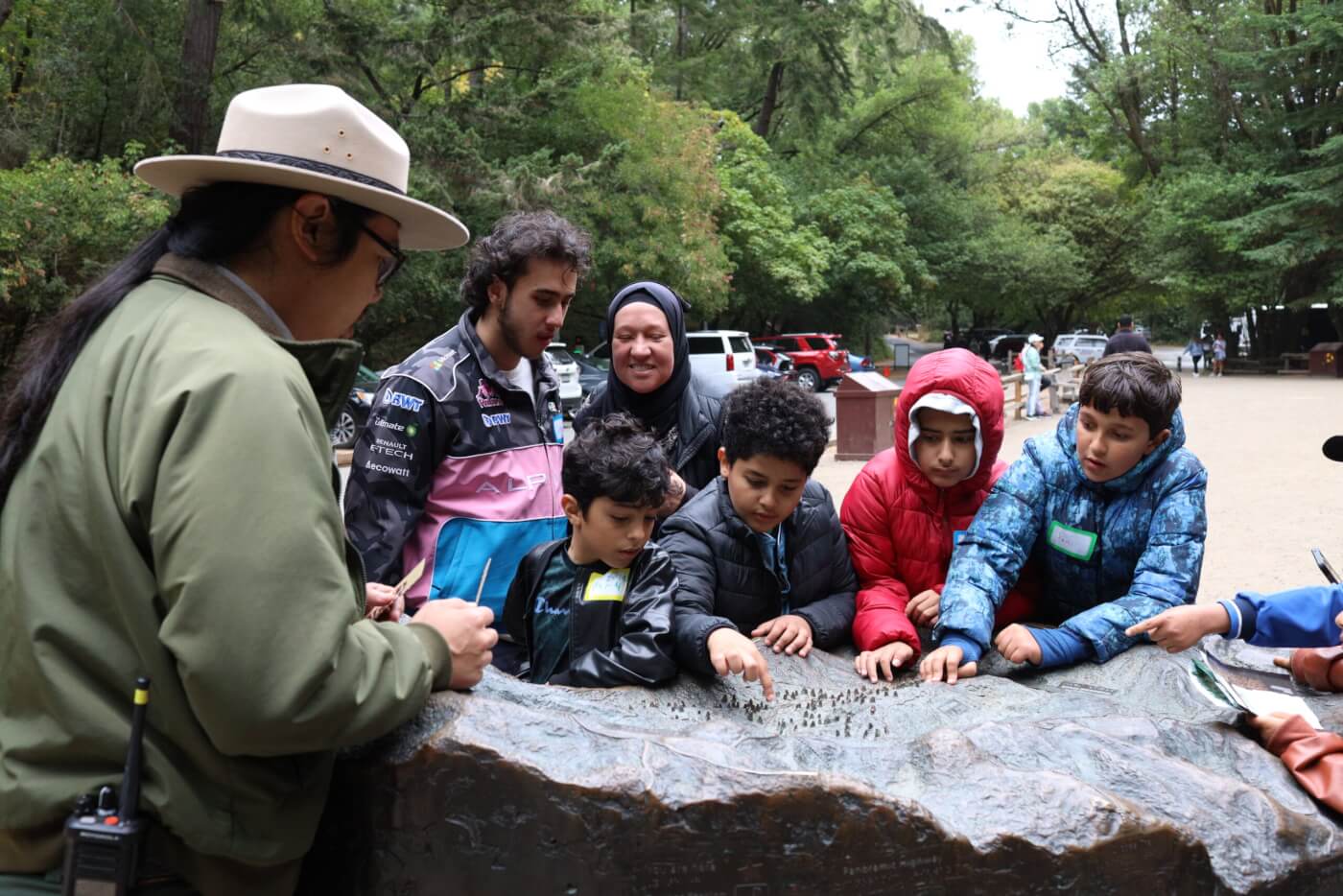 A park ranger shows a group of kids a raised map while they point and explore.