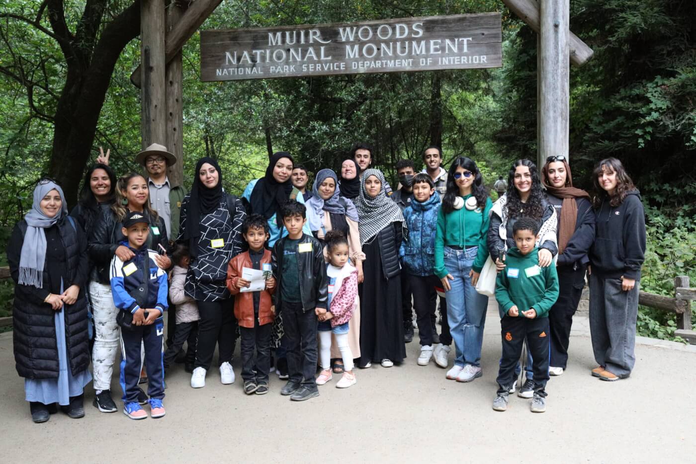 A group poses together under the Muir Woods National Monument sign.