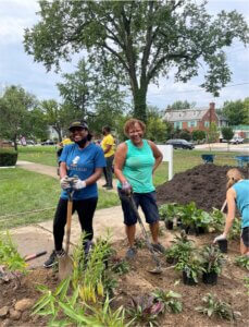 Volunteers smiling while planting flowers and gardening outdoors near a church lawn.