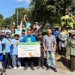 Large group of volunteers gathered outdoors with a Sacred Grounds native plants sign.