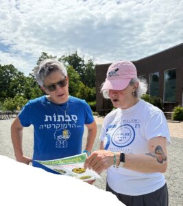 Two women reviewing a Sacred Grounds native planting flyer outdoors.