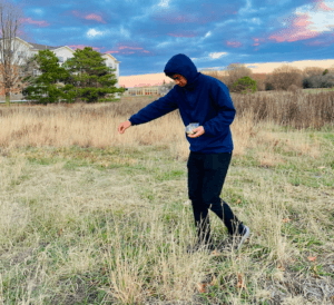 A program participant sprinkles seeds on a field. 
