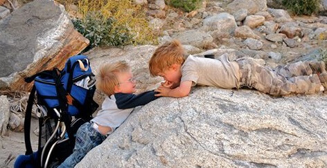 Boys helping each out climb rocks.