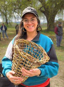 Portrait of Trelasa Baratta in front of a tree, smiling and holding a hand-woven basket.