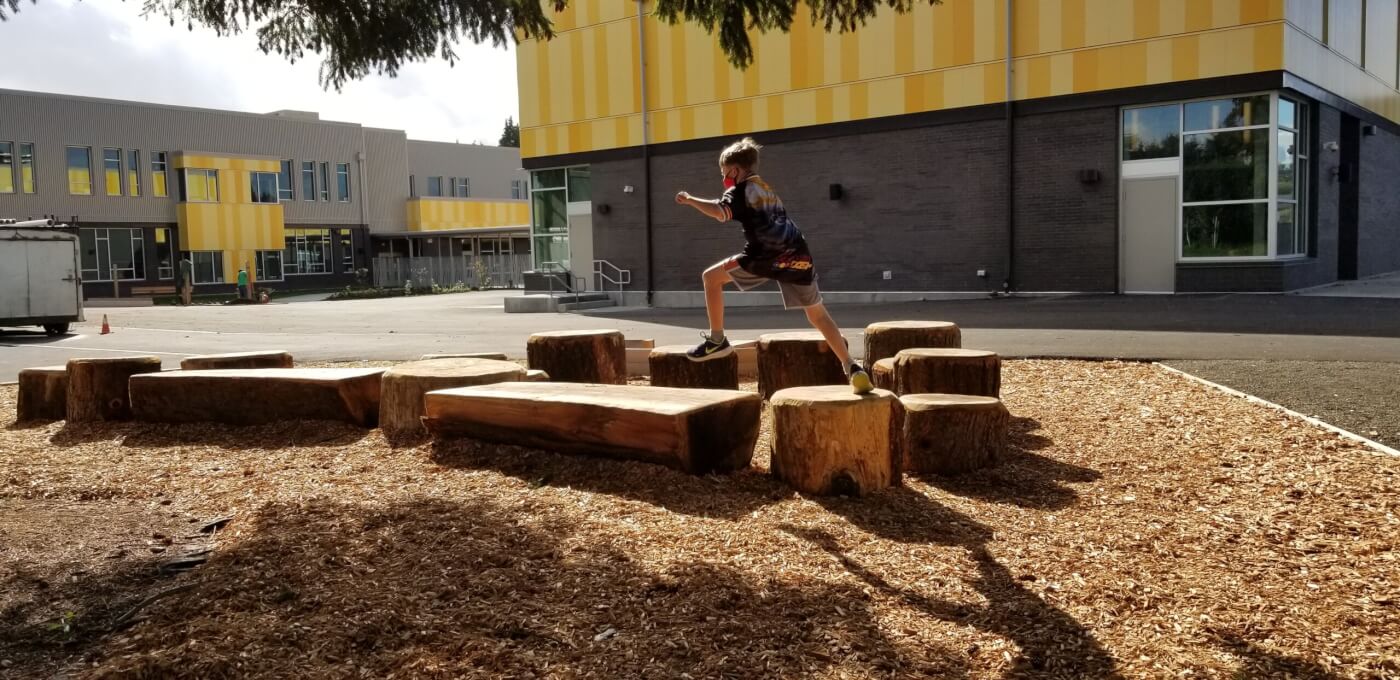 Child jumping across tree stumps on a school playground in sunlightChild jumping across tree stumps on a school playground in sunlight.