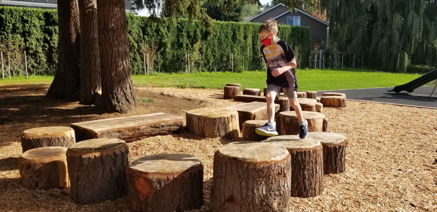 A young student runs across a group of tree stumps, all at different heights and widths.
