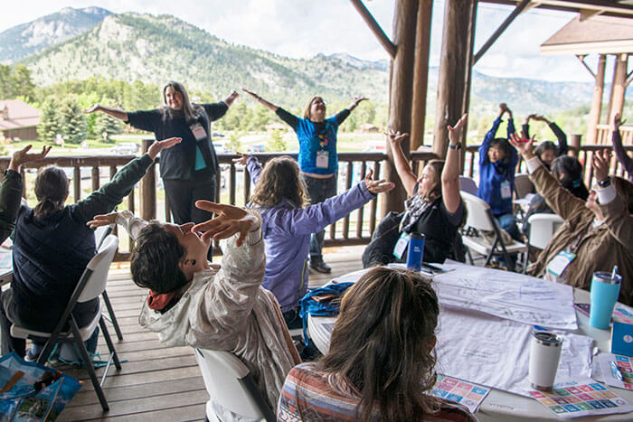Group sitting at tables holding out their hands in unison.
