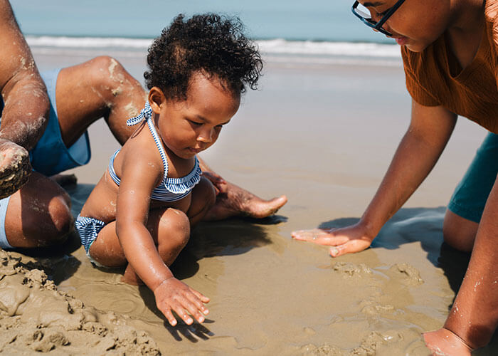 Child playing in the sand on a beach with parents.