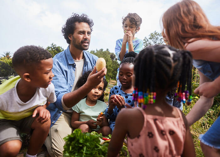 Adult showing kids a potato in a garden.