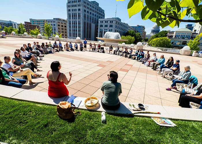 Group sitting in chairs in a circle outside listening to a speaker.