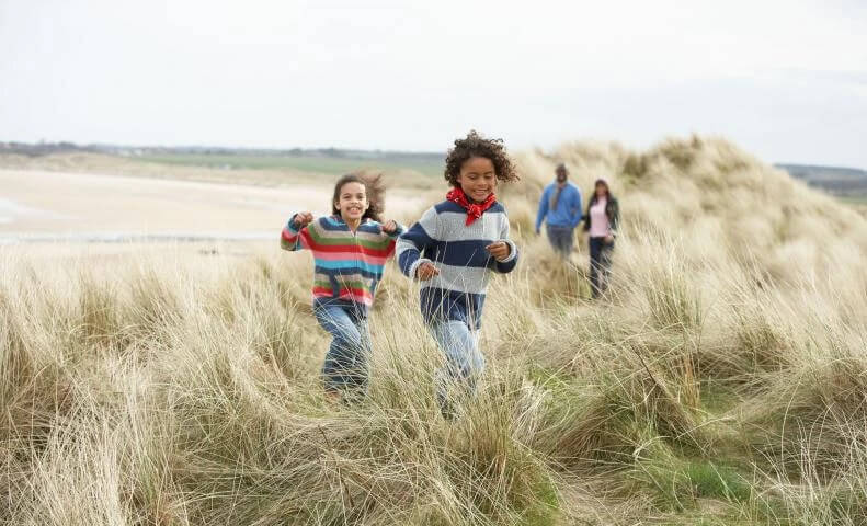 two kids running on beach sand dunes and parents trailing behind