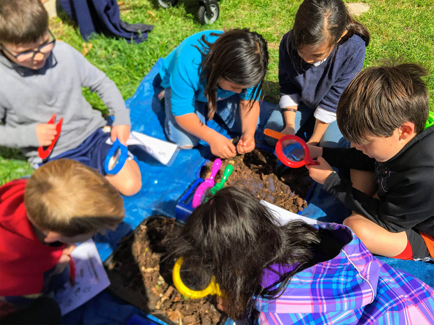Kids playing outside together with magnifying glasses.